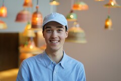 Unser Azubi guckt lächelnd zur Kamera. Hinter ihm hängen viele leuchtende Deckenlampen in verschiedenen Formen, die den Licht erhellen und für eine entspannende Stimmung sorgen