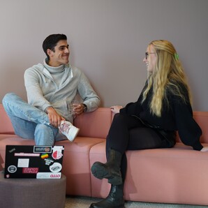 Drei junge Menschen sitzen in lockerer Haltung auf einer großen Couch und reden miteinander