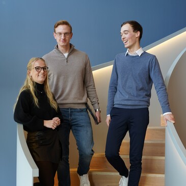 Drei Azubiblogger stehen auf einer geschwungenen, modernen Treppe