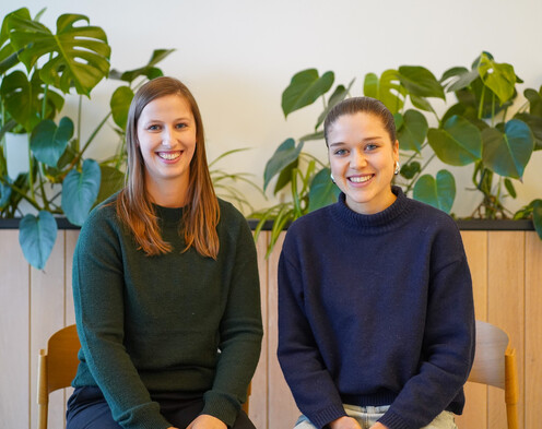Zwei weibliche Autorinnen vor einer Wand mit Pflanzen in warmem Licht