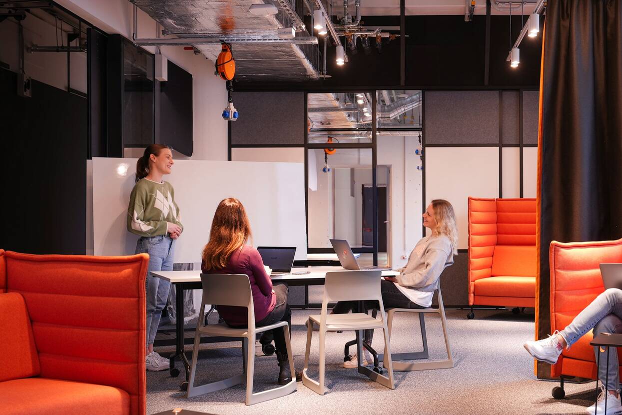 In der Projektgarage, in der sich mehrere Kollegen und Kolleginnen von OTTO befinden, die sich austauschen und arbeiten, stehen viele verschiedene bunte Sessel, Tische, Stühle und Whiteboards.