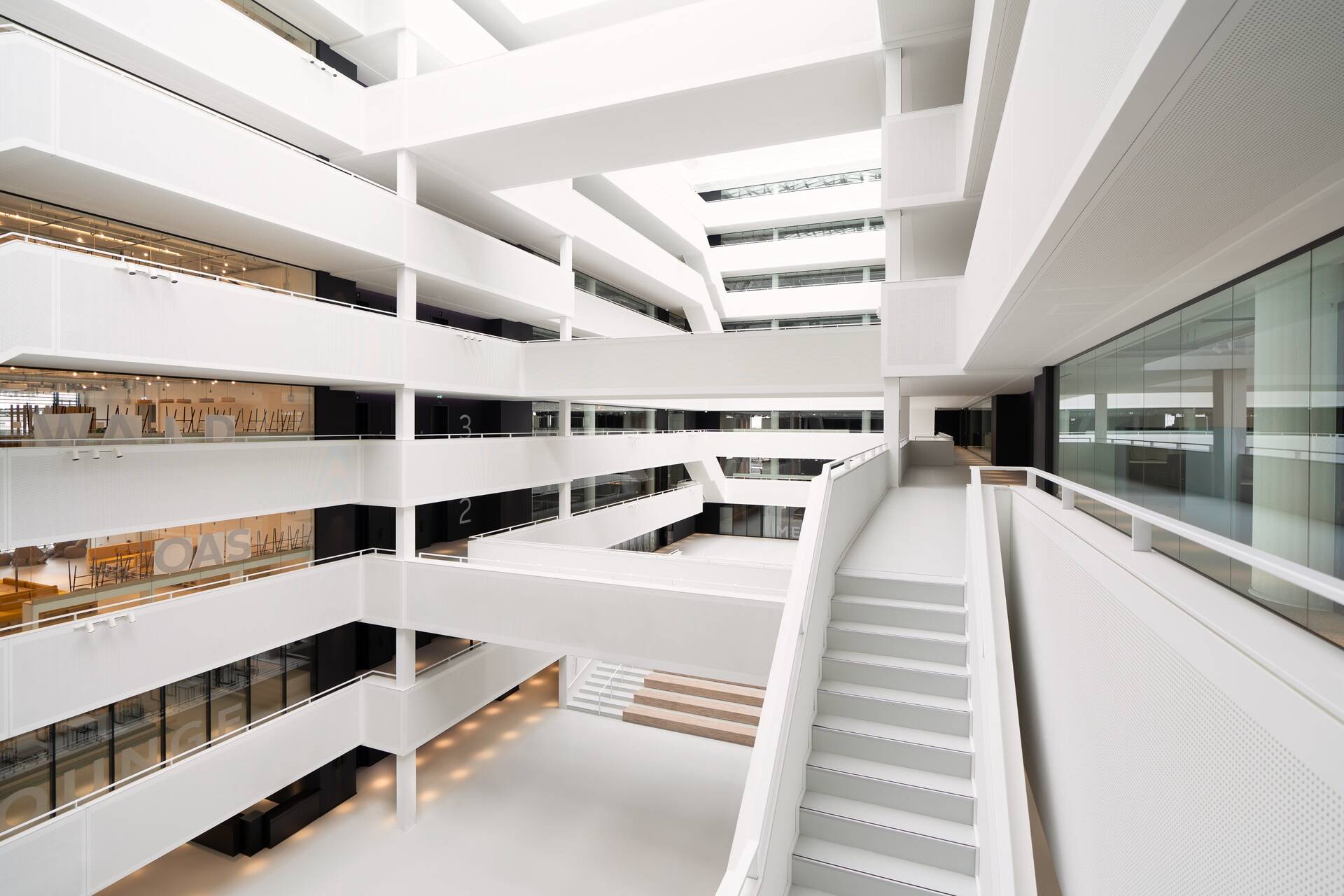 Das lichtdurchflutete Atrium im OTTO-Headquarter. Unten befindet sich der Eingang und Sitzreihen für Vorträge und Veranstaltungen. Die Mitte des Gebäudes ist offen, die Arbeitsflächen und Räumlichkeiten befinden sich am Rand des Gebäudes. 
