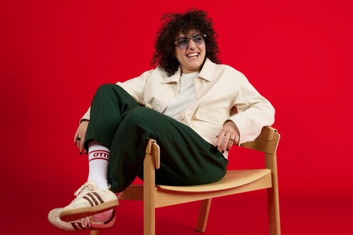 Unsere Kollegin sitzt lässig auf dem Stuhl Unsere Führungskraft aus dem Risikomanagement sitzt sehr entspannt auf einem Stuhl vor einem roten Hintergrund. Ihre Beine lässt sie über die Stuhllehne baumeln. Sie trägt eine Sonnenbrille und lächelt in die Kamera.