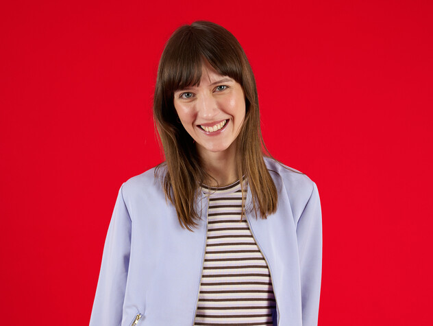 Unsere Kollegin aus Strategie lächelt in die Kamera Unsere Kollegin aus Strategie ist ein Teil beim Living Red Shooting. Sie steht vor einem roten Hintergrund und lächelt in die Kamera.