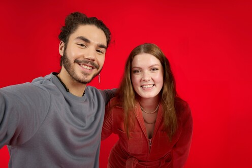 Zwei Kollegen von OTTO umarmen sich lächelnd und stehen vor einem roten Hintergrund.