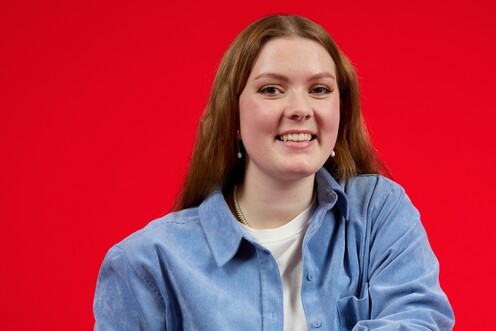 Duale Studentin auf einem Stuhl sitzend Duale Studentin in Business Administration sitzt auf einem umgedrehten Stuhl und lächelt in die Kamera. In ihrer linken Hand hält sie Kopfhörer.