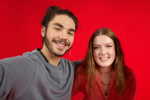 Zwei Kollegen von OTTO umarmen sich lächelnd und stehen vor einem roten Hintergrund.