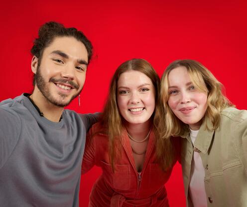 Unsere Azubis machen ein Selfie. Sie stehen vor einem roten Hintergrund und lächeln in die Kamera. 