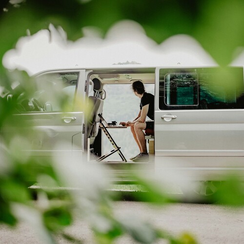 Ein weißer Van, in dem zwei Personen sitzen und auf die Berge schauen.