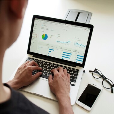 Eine Person arbeitet am Laptop. Neben dem Laptop liegen Handy und Brille.