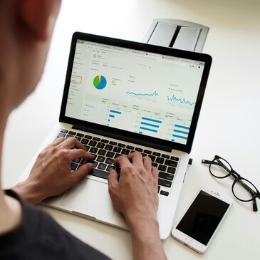 Eine Person arbeitet am Laptop. Neben dem Laptop liegen Handy und Brille.