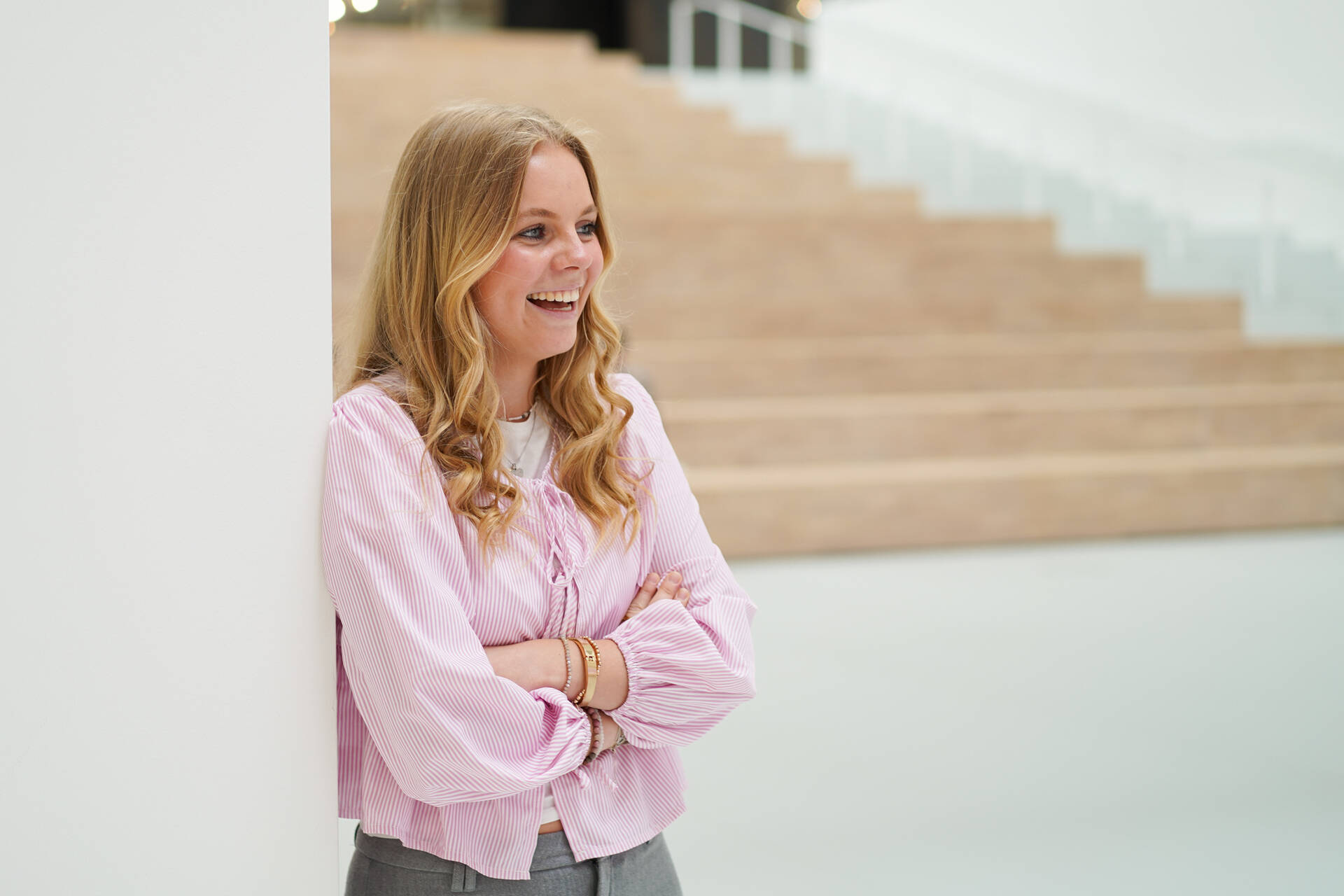 Werkstudentin hat die Arme verschränkt und lacht herzlich zur Seite und befindet sich im Atrium.