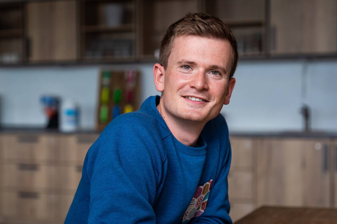 Unser Kollege Lead Product Manager Apps sitzt an einem Tisch  und lehnt sich nach vorne und blickt zur Kamera