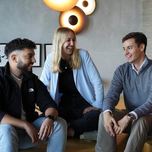 Drei Azubis sitzen zusammen auf dem Sofa reden und lachen gemeinsam.