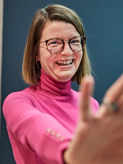 Eine Kollegin mit Brille und schulterlangen Haaren lächelt in die Kamera.