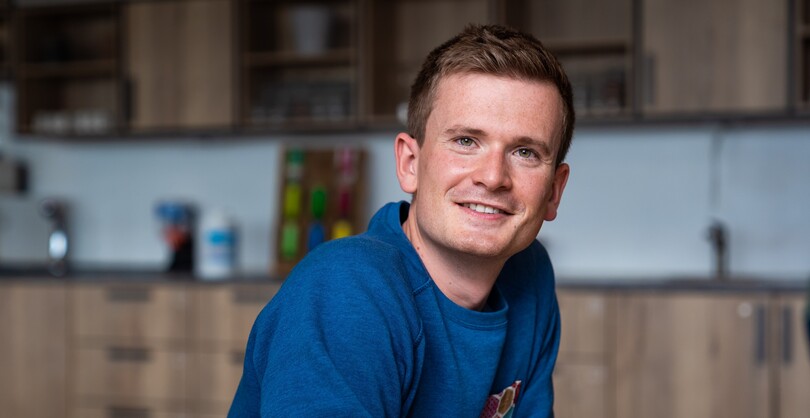 Unser Kollege Lead Product Manager Apps sitzt an einem Tisch  und lehnt sich nach vorne und blickt zur Kamera