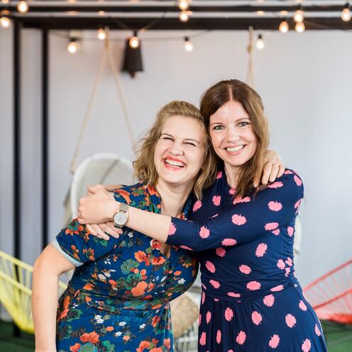 m Hintergrund von Lichterketten umarmen sich zwei Mitarbeiterinnen aus dem Recruitment herzlich im Social Space.