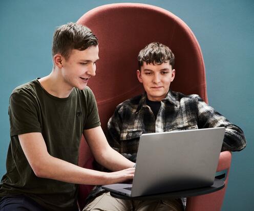 Zwei Azubis sitzen am Laptop Zwei Azubis sitzen auf einem roten Sofa konzentriert am Laptop. Im Hintergrund ist eine blaue Wand zusehen.