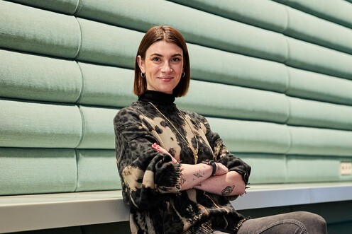 Unsere Kollegin sitzt mit verschränkten Armen auf dem Stuhl. und lächelt in die Kamera.