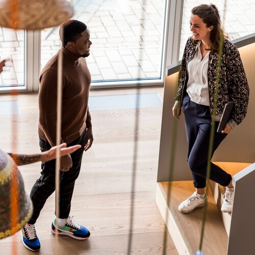 Gespräch zwischen Kollegen Zwei Kollegen und eine Kollegin unterhalten sich begeistert in einem der OTTO Gebäude. Die Kollegin steht auf der Treppe.