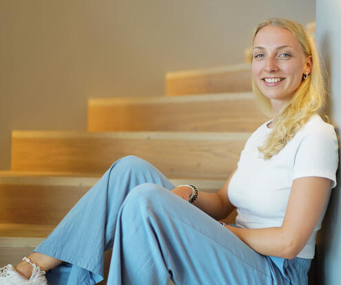Eine Praktikantin sitzt auf einer Treppenstufe und lehnt sich an und lächelt in die Kamera.