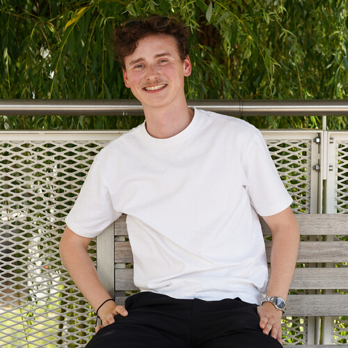 Unser Kollege aus dem Advertising-Team sitzt lächelnd auf einer Bank auf dem Otto Campus, die Hände in den Hosentaschen.