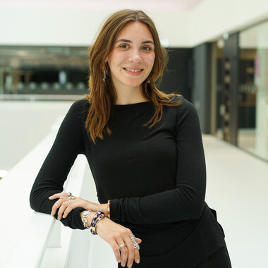 Werkstudentinim Bereich Retail & Marketplace Unsere Werkstudentin steht im Atrium auf dem Campus. Sie lächelt in die Kamera.