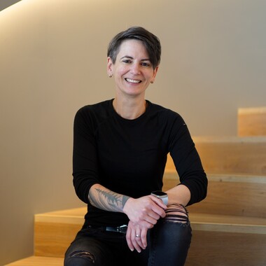Fronted Developerin, Role Model in Tech Sie sitzt locker auf der Treppe in einem Gebäude des OTTO Campus. Sie ist als Frontend Developerin Teil der ersten Staffel Role Models in Tech.