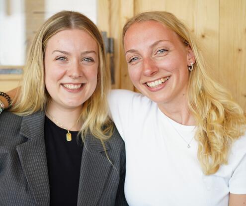 Zu Kolleginen umarmen sich herzlich Zwei Kolleginnen stehen lächelnd nebeneinander und die eine legt die Hand über die Schulter der anderen.