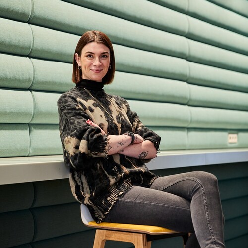 Unsere Kollegin sitzt mit verschränkten Armen auf dem Stuhl. und lächelt in die Kamera.