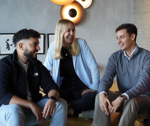 Drei Azubis sitzen zusammen auf dem Sofa reden und lachen gemeinsam.