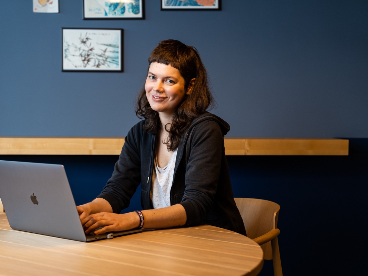 Softwareentwicklerin sitzt mit Laptop am Tisch und lächelt in die Kamera