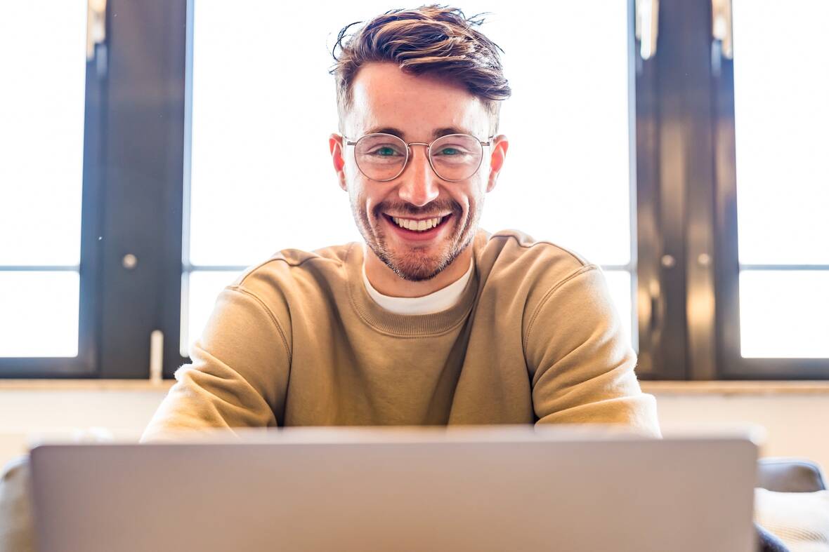 Ein Kollege aus dem UX Design schaut lächelnd auf seinen Laptop.