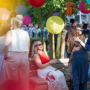 Viele Menschen, umgeben von farbenfrohen Lampions, stehen bei gutem Wetter in guter Stimmung zusammen. Einige unterhalten sich mit einer Flasche in der Hand. Im Hintergrund tummeln viele Menschen umher und genießen auch die Feierlichkeiten für das 75-jährige Bestehen des OTTO-Versandhandels