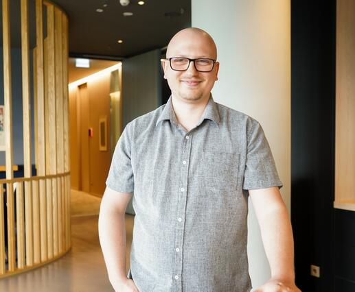 Anwendungsentwickler bei OTTO steht im Social Space Anwendungsentwickler bei OTTO steht im Social Space. Er lächelt in die Kamera und stützt sich lässig am Tisch ab.