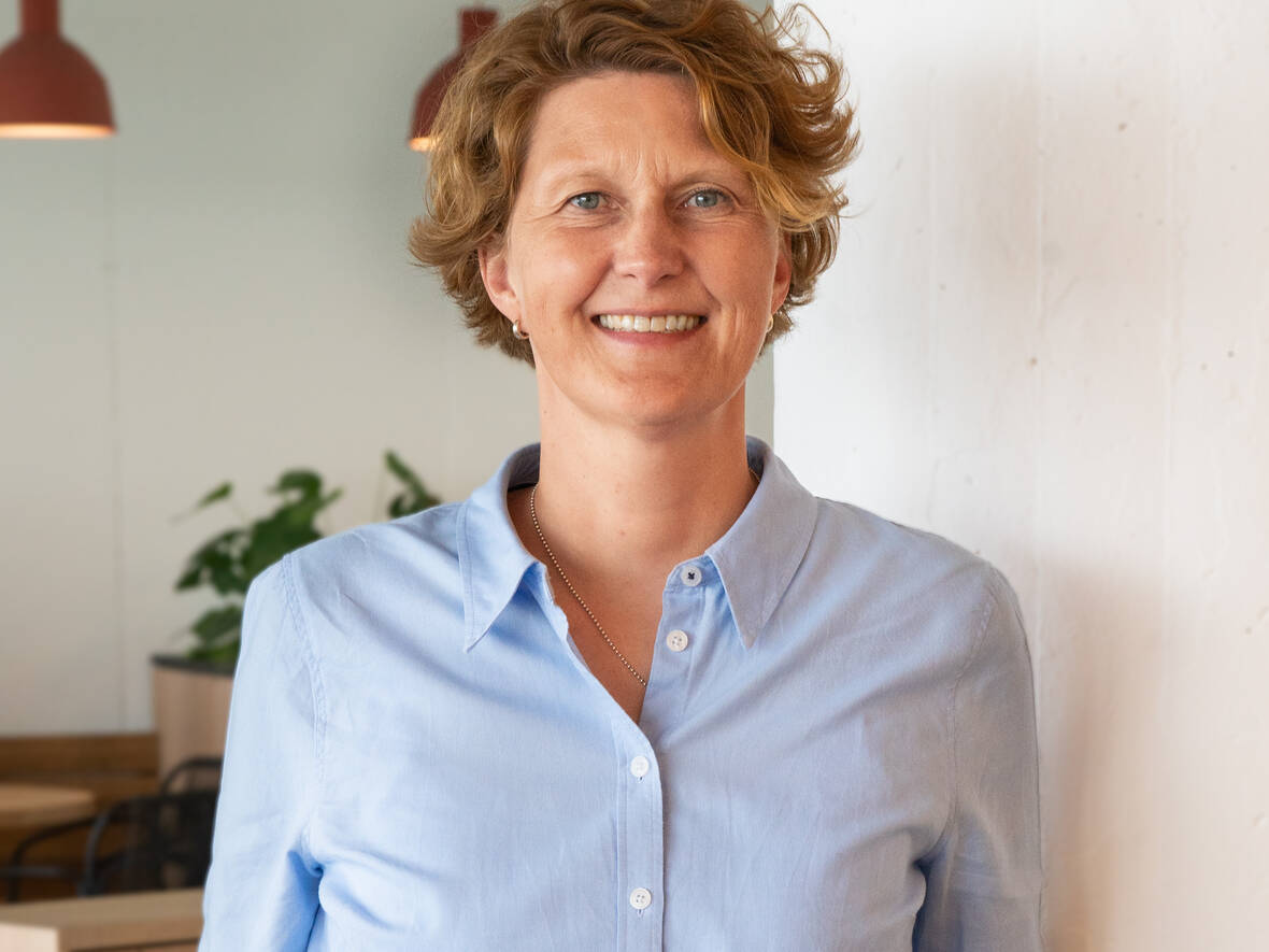 Führungskraft im Bereich Unternehmensstrategie steht im Social Space hat die Hände in der Hose und lächelt in die Kamera