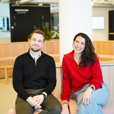 Unsere Kollegen lächeln in die Kamera Unsere Kollegen sitzen auf einer Bank im Social Space und lächeln in die Kamera.