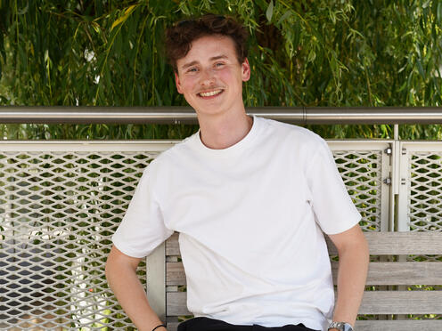 Unser Kollege aus dem Advertising-Team sitzt lächelnd auf einer Bank auf dem Otto Campus, die Hände in den Hosentaschen.