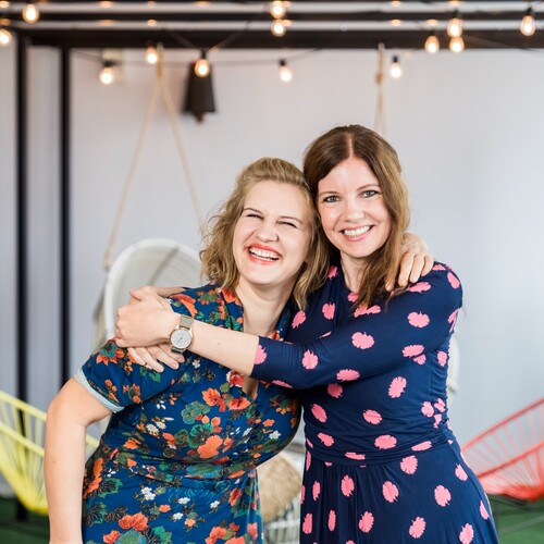 m Hintergrund von Lichterketten umarmen sich zwei Mitarbeiterinnen aus dem Recruitment herzlich im Social Space.