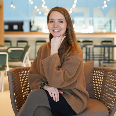 Mentorin bei OTTO sitzt auf einem Sthul Mentorin im Mentoring Programm bei OTTO. Sie sitzt lächelnd auf einem Stuhl im Social Space in unserem Headquarter Gebäude von OTTO