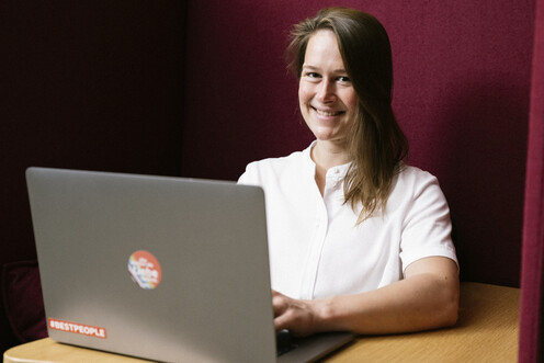 Kollegin aus Data Scientist sitzt lächelnd am Laptop in einer gemütlichen, gepolsterten Ecke bei OTTO