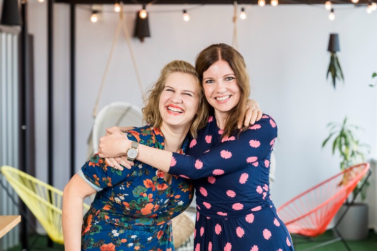 m Hintergrund von Lichterketten umarmen sich zwei Mitarbeiterinnen aus dem Recruitment herzlich im Social Space.