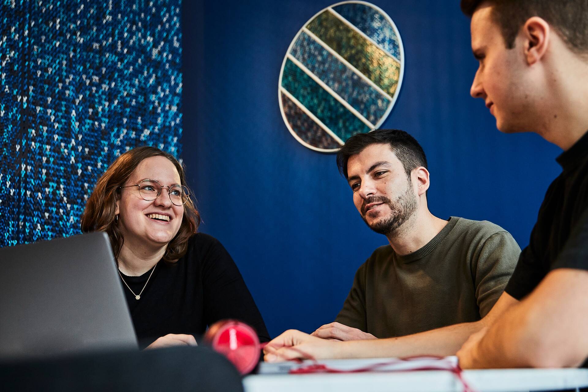 Drei Kollegen sitzen am Tisch mit ihrem Laptop und unterhalten sich im Social Space.