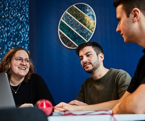 Drei Kollegen sitzen am Tisch mit ihrem Laptop und unterhalten sich im Social Space.
