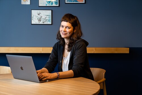 Softwareentwicklerin sitzt mit Laptop am Tisch und lächelt in die Kamera