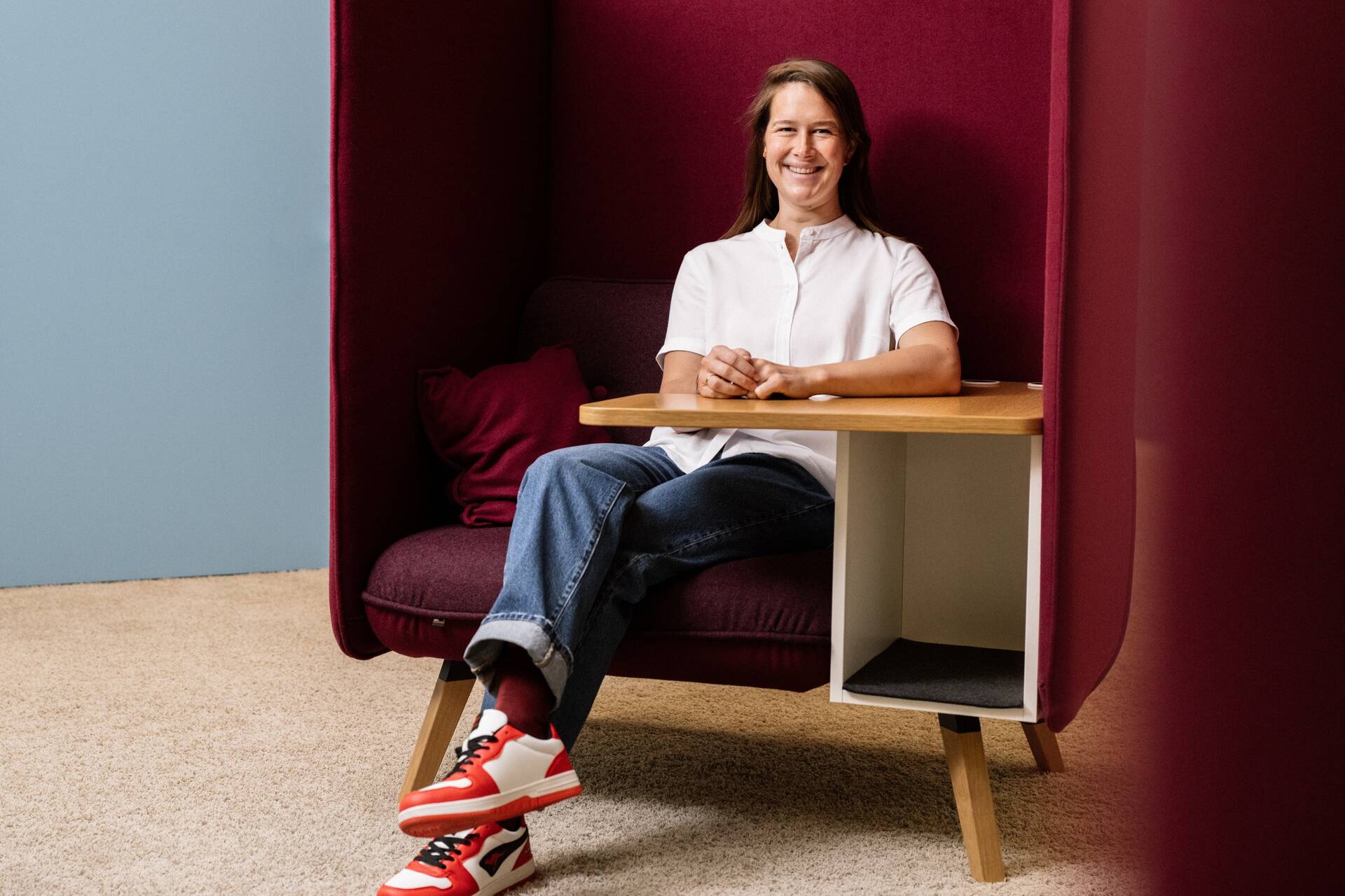 Unsere Kollegin sitzt in einer gepolsterten Ecke mit überschlagenen Beinen und den Händen auf dem Tisch. 