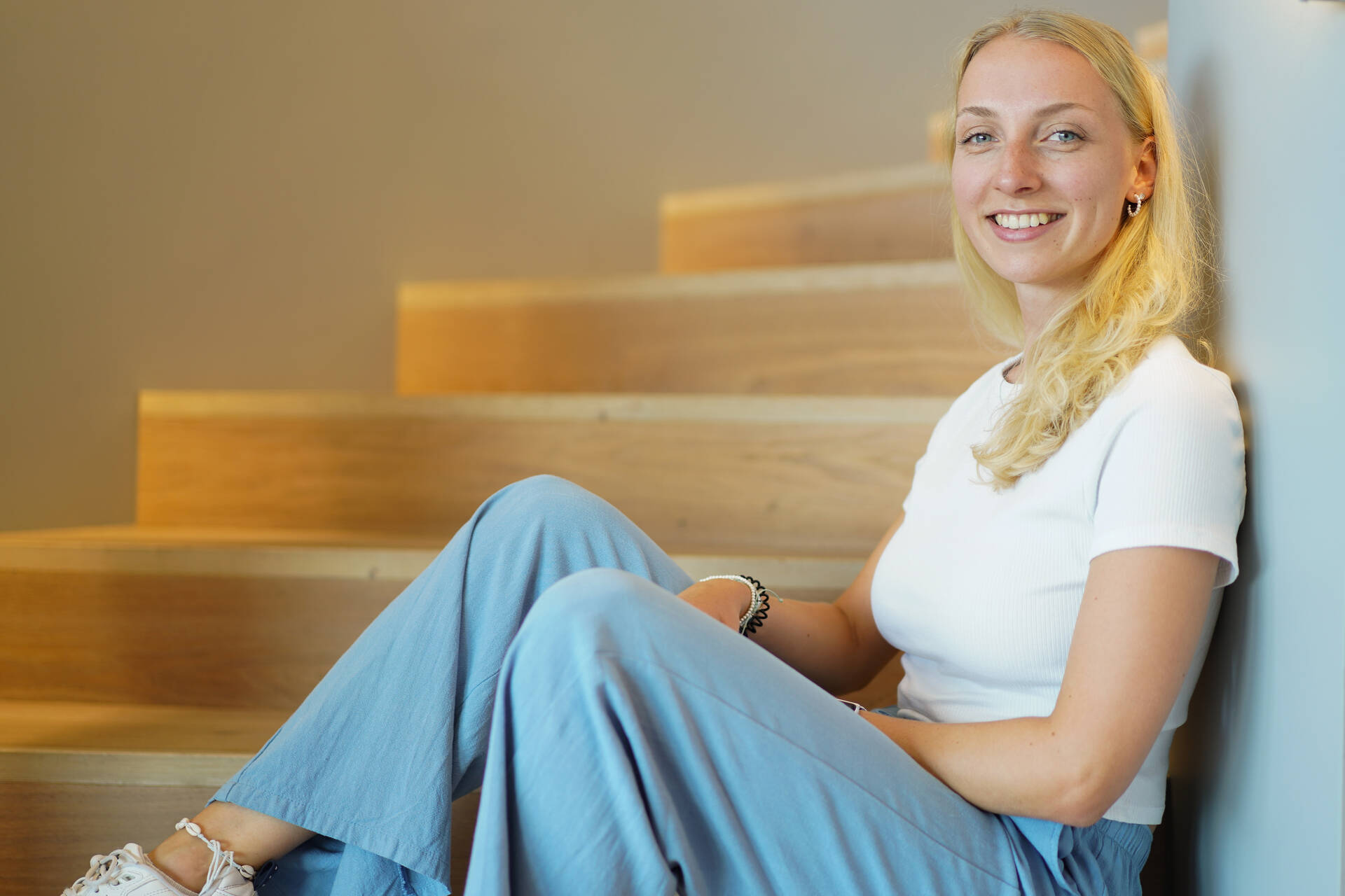 Eine Praktikantin sitzt auf einer Treppenstufe und lehnt sich an und lächelt in die Kamera.