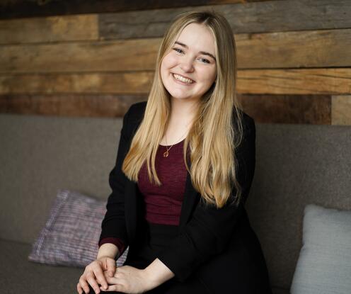 Junior HR Managerin sitzt auf einem Sofa und hat die Beine überschlagen und lächelt in die Kamera.