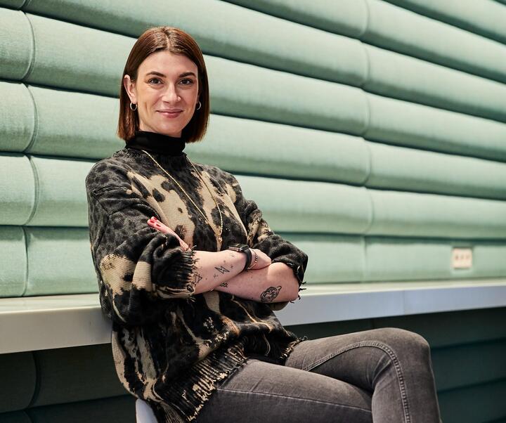 Unsere Kollegin als Venture Client Lead, Startup-Kooperationsmanagerin Unsere Kollegin sitzt mit verschränkten Armen auf dem Stuhl. und lächelt in die Kamera.