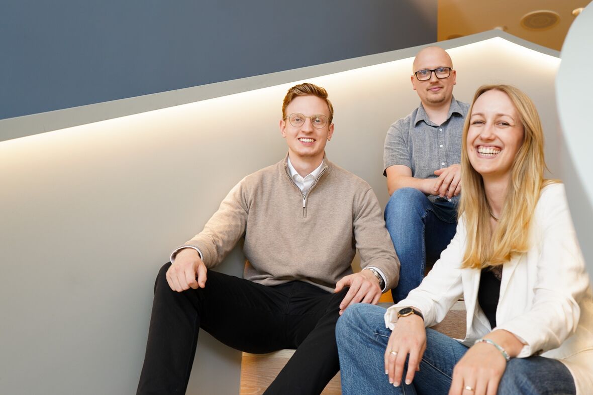 Drei Kollegen sitzen auf der Treppe und lächeln in die Kamera.